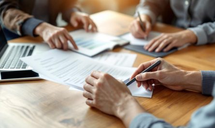 Équipe d’une PME digitale préparant un déplacement professionnel : documents d’assurance et ordinateur sur une table de réunion, ambiance de travail en salle moderne.