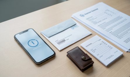 Enveloppe de transfert d’argent non ouverte posée à côté d’un smartphone et d’un portefeuille sur un bureau lumineux.